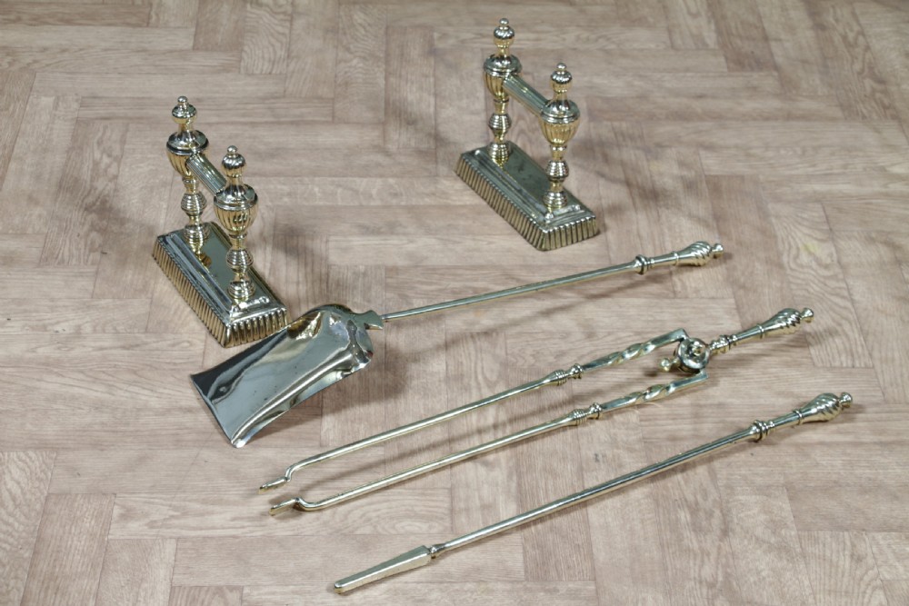 A late Victorian polished brass companion set featuring a shovel, tongs, and poker supported horizontally across two urn-topped brass firedogs. View VI
