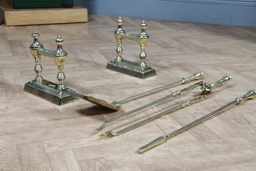 A late Victorian polished brass companion set featuring a shovel, tongs, and poker supported horizontally across two urn-topped brass firedogs. View IX