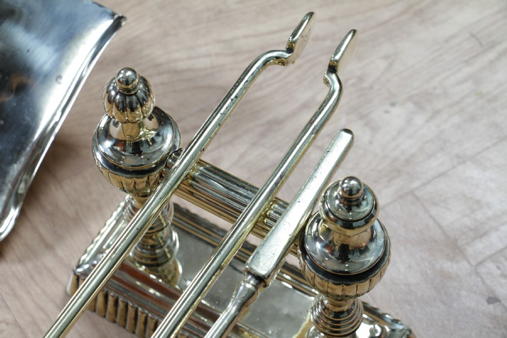 A late Victorian polished brass companion set featuring a shovel, tongs, and poker supported horizontally across two urn-topped brass firedogs. View XI