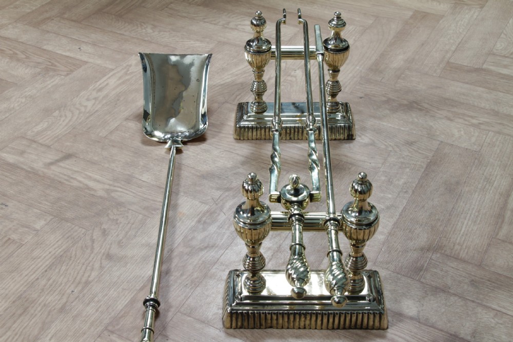 A late Victorian polished brass companion set featuring a shovel, tongs, and poker supported horizontally across two urn-topped brass firedogs. View XIV