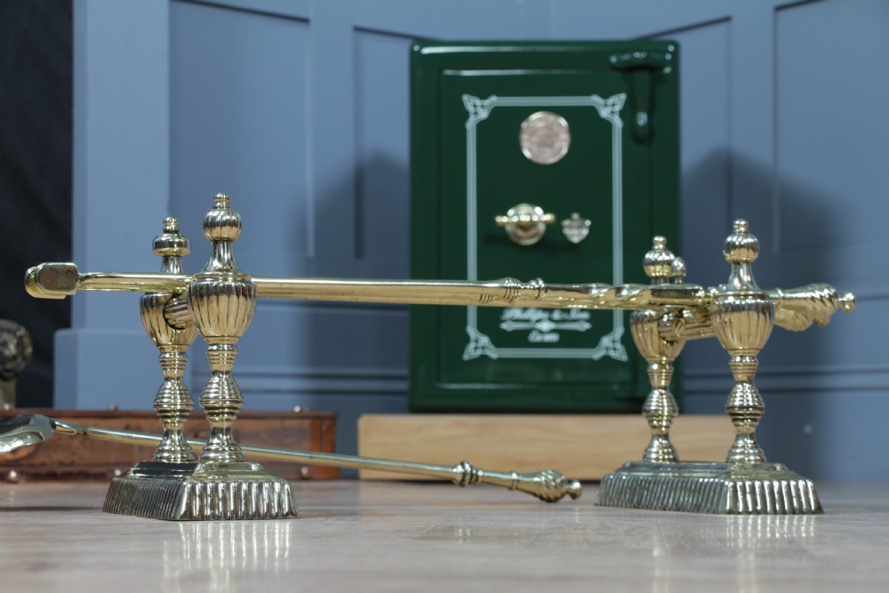 A late Victorian polished brass companion set featuring a shovel, tongs, and poker supported horizontally across two urn-topped brass firedogs. View XVI