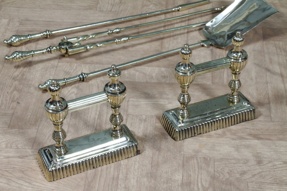 A late Victorian polished brass companion set featuring a shovel, tongs, and poker supported horizontally across two urn-topped brass firedogs. View XIX