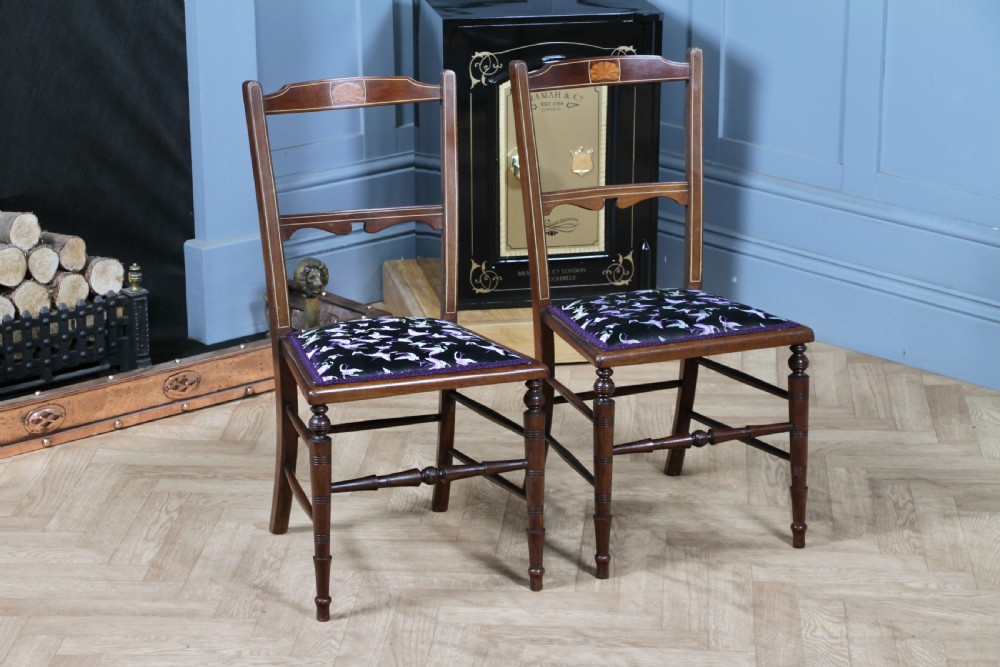 A pair of antique Edwardian mahogany side chairs featuring inlaid shell cresting, slender horizontal splats, turned legs, and dark silk patterned seats.