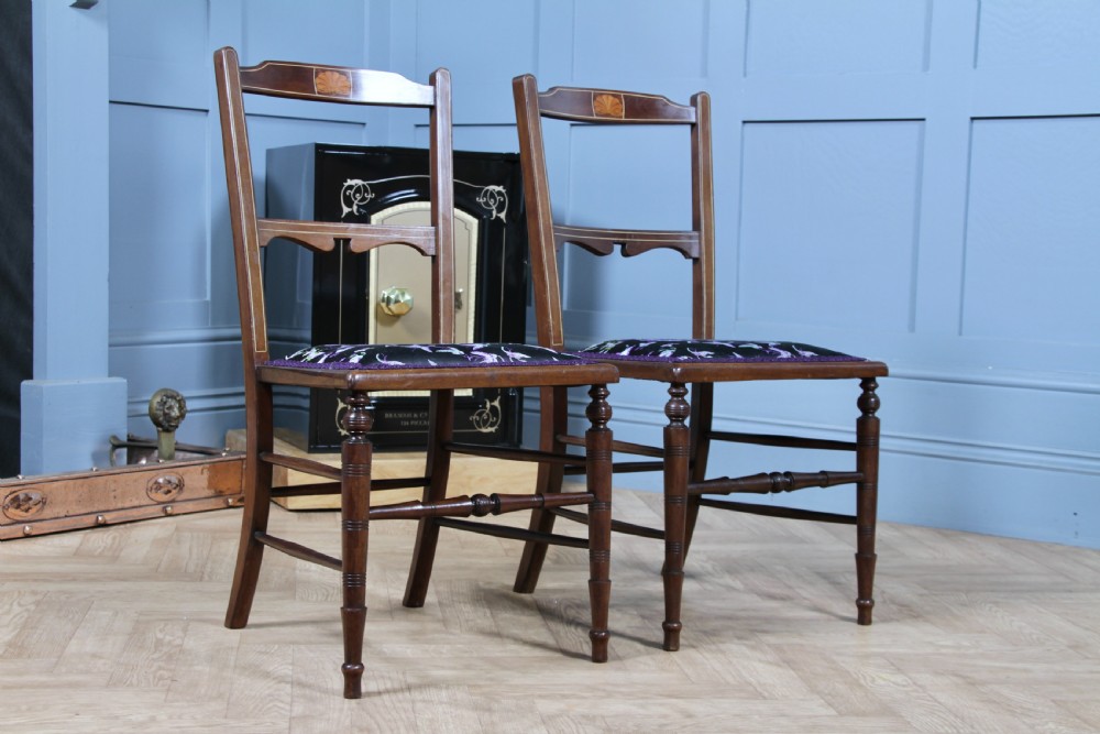 A pair of antique Edwardian mahogany side chairs featuring inlaid shell cresting, slender horizontal splats, turned legs, and dark silk patterned seats. View II