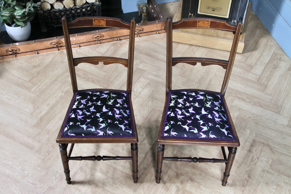 A pair of antique Edwardian mahogany side chairs featuring inlaid shell cresting, slender horizontal splats, turned legs, and dark silk patterned seats. View V