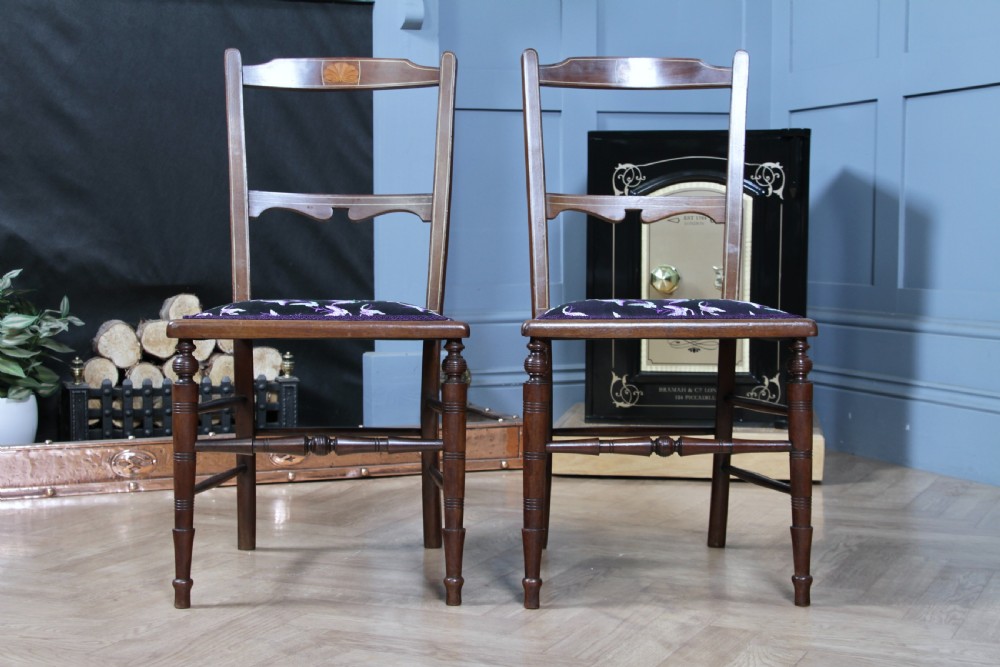 A pair of antique Edwardian mahogany side chairs featuring inlaid shell cresting, slender horizontal splats, turned legs, and dark silk patterned seats. View VI