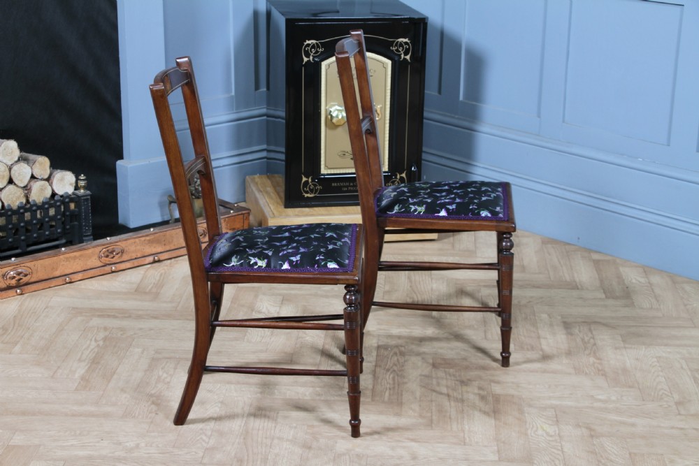 A pair of antique Edwardian mahogany side chairs featuring inlaid shell cresting, slender horizontal splats, turned legs, and dark silk patterned seats. View X
