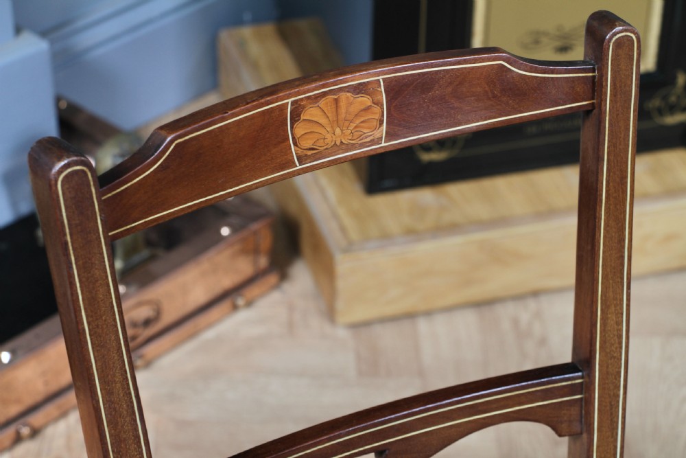 A pair of antique Edwardian mahogany side chairs featuring inlaid shell cresting, slender horizontal splats, turned legs, and dark silk patterned seats. View XIV