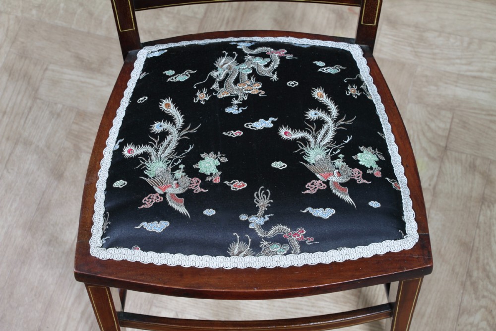 An Edwardian mahogany nursing chair featuring an inlaid pierced back splat, decorative stringing, and a black silk upholstered seat with embroidered floral motifs. View IX