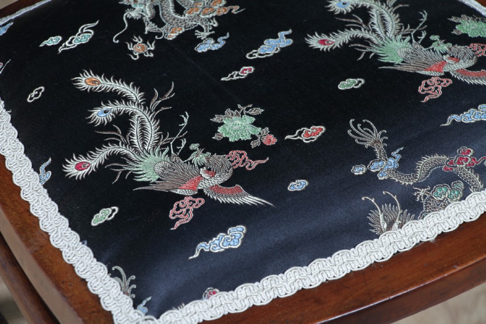 An Edwardian mahogany nursing chair featuring an inlaid pierced back splat, decorative stringing, and a black silk upholstered seat with embroidered floral motifs. View X