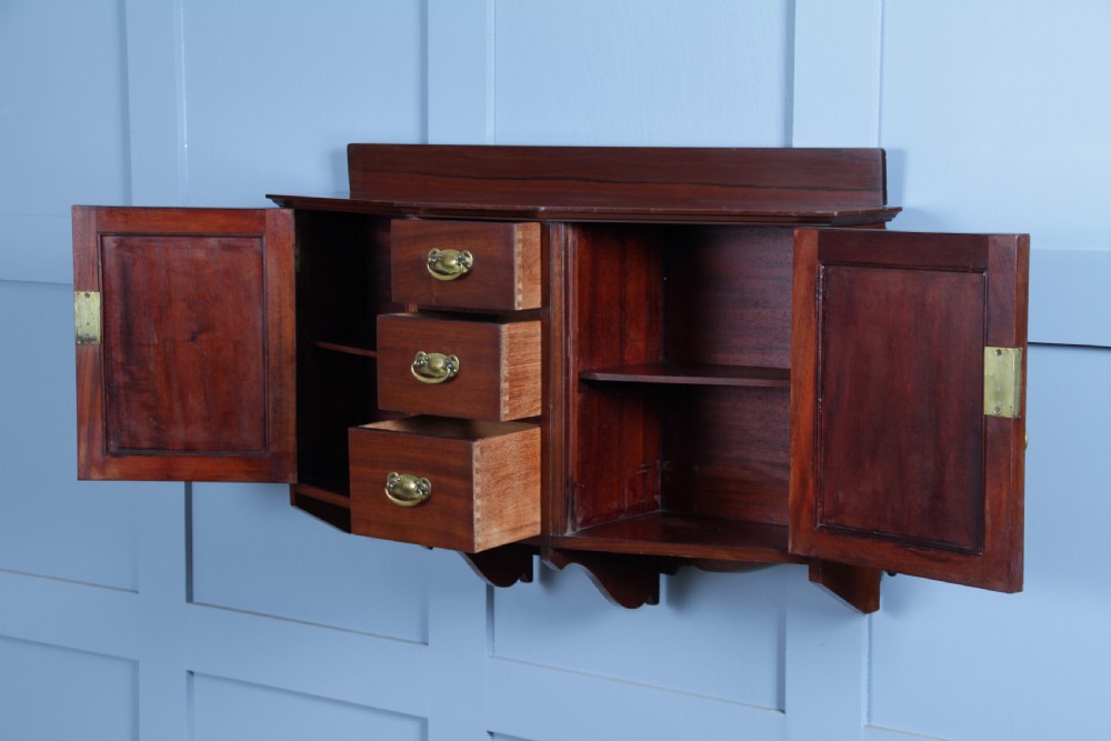 A small Edwardian mahogany wall hanging cabinet featuring two outer cupboards, three central drawers, brass handles, and a low back gallery. View IV