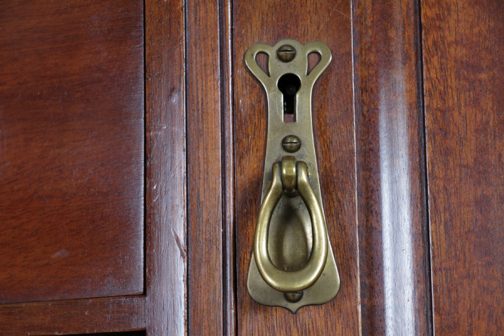 A small Edwardian mahogany wall hanging cabinet featuring two outer cupboards, three central drawers, brass handles, and a low back gallery. View IX