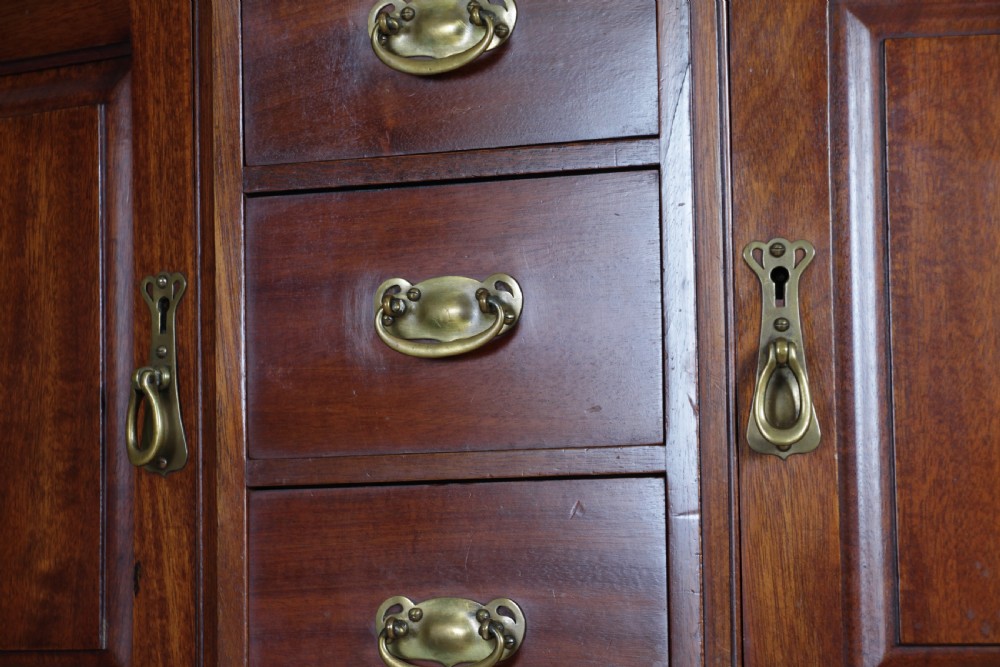 A small Edwardian mahogany wall hanging cabinet featuring two outer cupboards, three central drawers, brass handles, and a low back gallery. View X