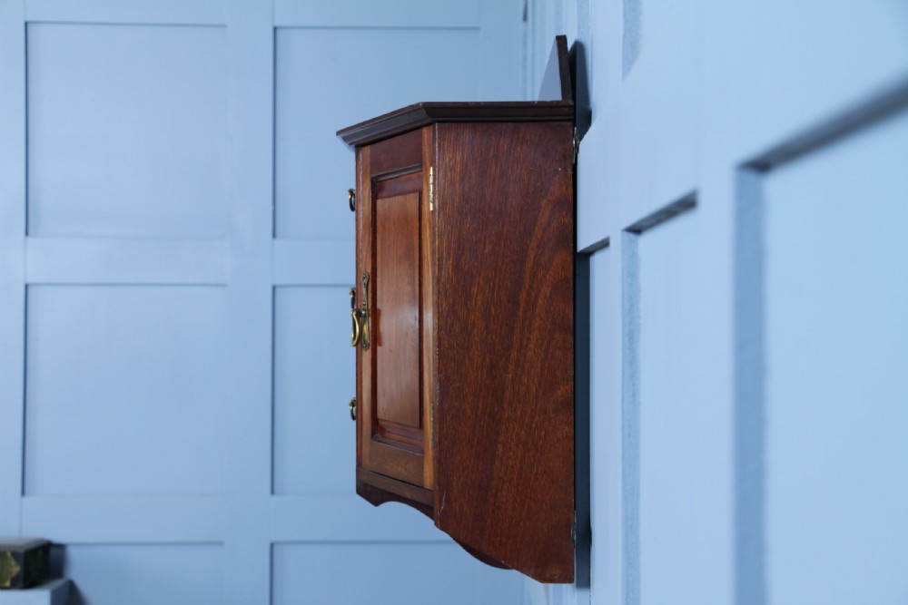 A small Edwardian mahogany wall hanging cabinet featuring two outer cupboards, three central drawers, brass handles, and a low back gallery. View XI