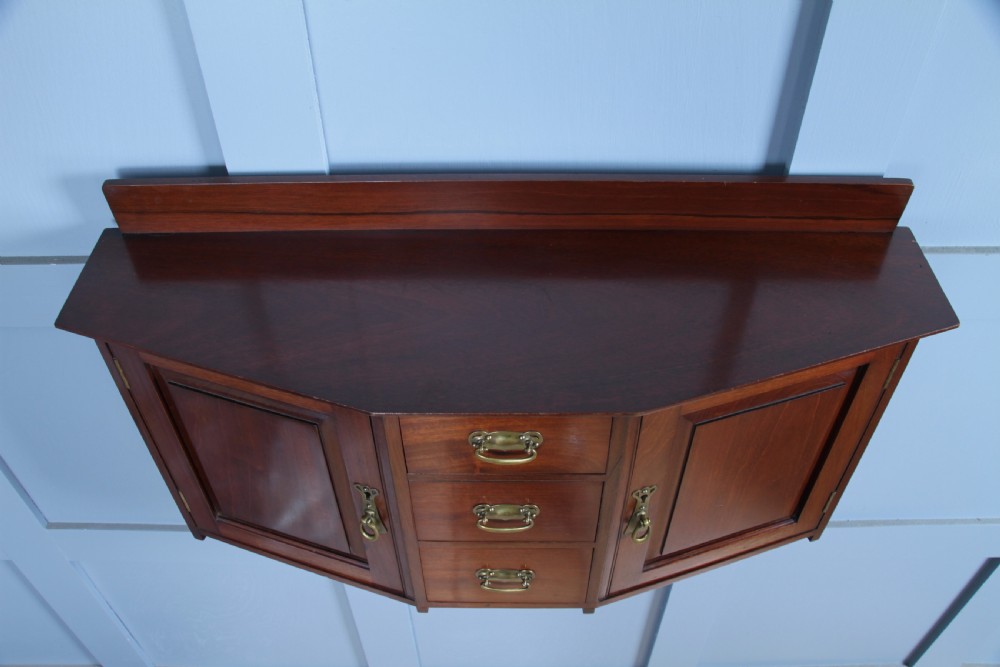 A small Edwardian mahogany wall hanging cabinet featuring two outer cupboards, three central drawers, brass handles, and a low back gallery. View XII