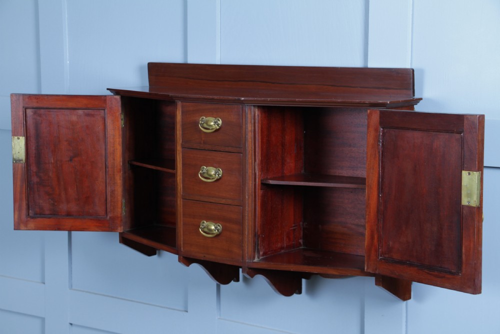 A small Edwardian mahogany wall hanging cabinet featuring two outer cupboards, three central drawers, brass handles, and a low back gallery. View XIII