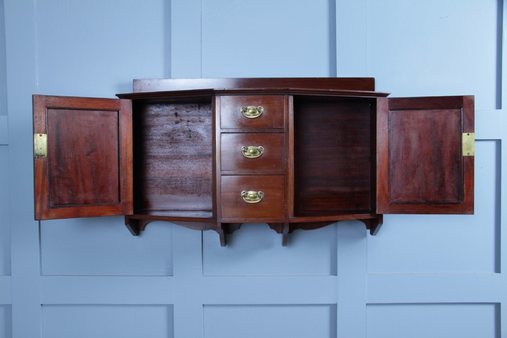 A small Edwardian mahogany wall hanging cabinet featuring two outer cupboards, three central drawers, brass handles, and a low back gallery. View XIV