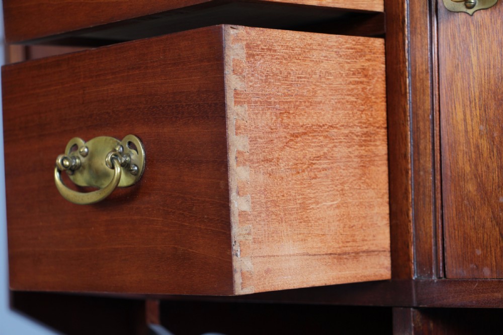 A small Edwardian mahogany wall hanging cabinet featuring two outer cupboards, three central drawers, brass handles, and a low back gallery. View XVI