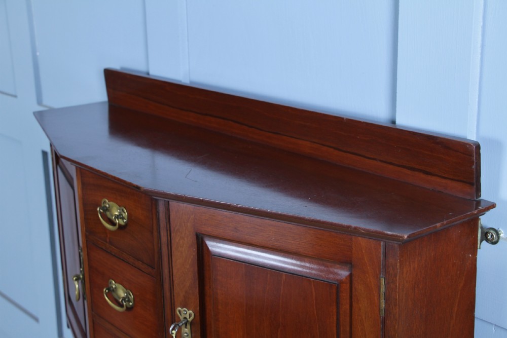A small Edwardian mahogany wall hanging cabinet featuring two outer cupboards, three central drawers, brass handles, and a low back gallery. View XVII