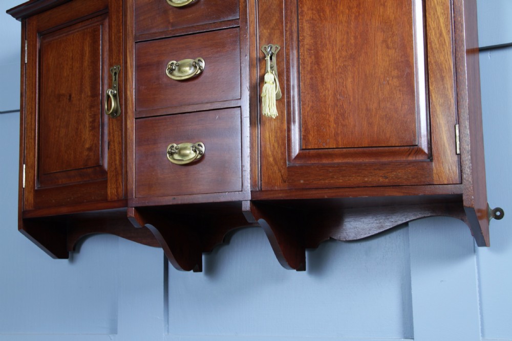 A small Edwardian mahogany wall hanging cabinet featuring two outer cupboards, three central drawers, brass handles, and a low back gallery. View XIX