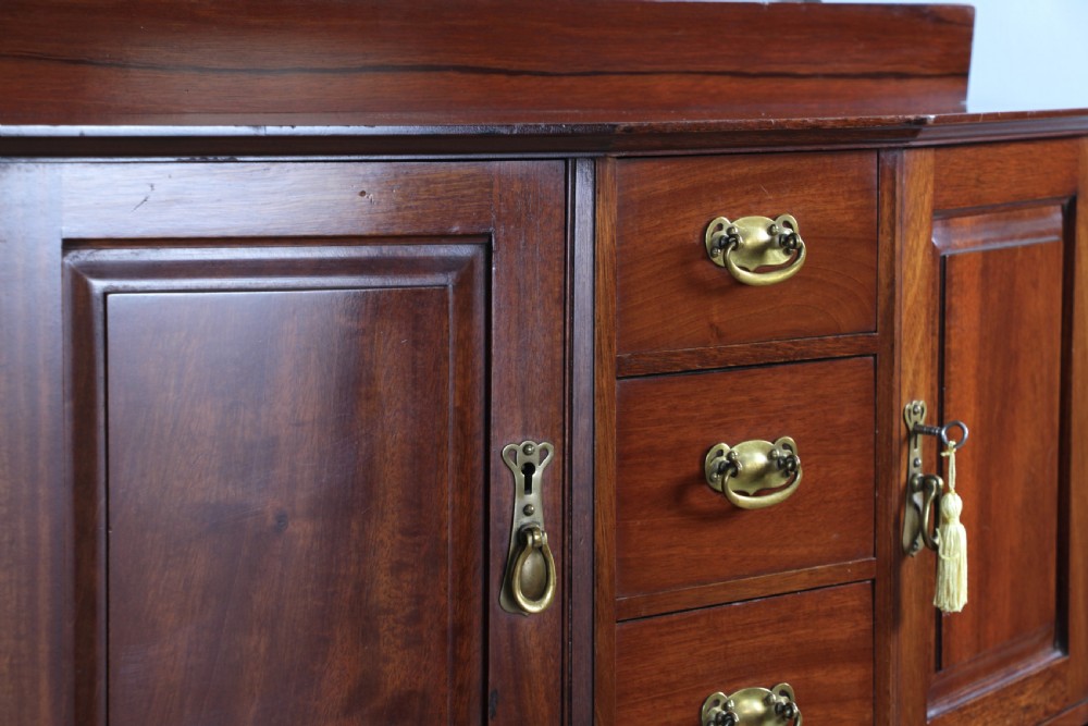 A small Edwardian mahogany wall hanging cabinet featuring two outer cupboards, three central drawers, brass handles, and a low back gallery. View XX