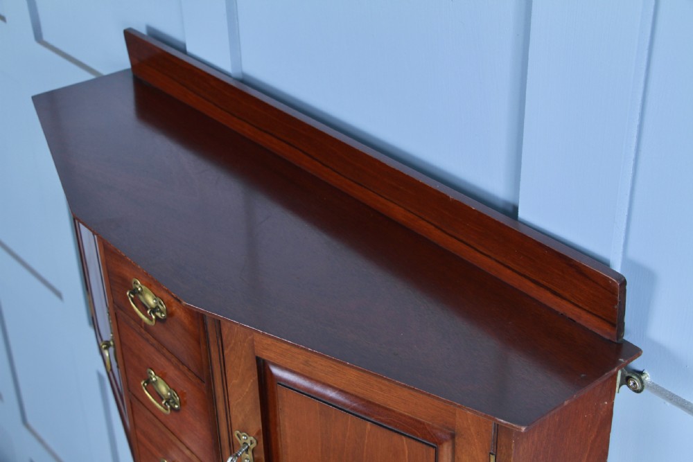 A small Edwardian mahogany wall hanging cabinet featuring two outer cupboards, three central drawers, brass handles, and a low back gallery. View XXI