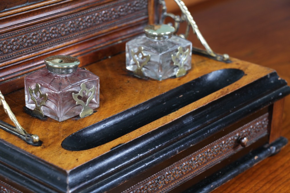 An Edwardian wooden inkstand featuring two glass inkwells, a shaped back gallery with finials, brass side supports, a pen groove, and a lower drawer. View IX