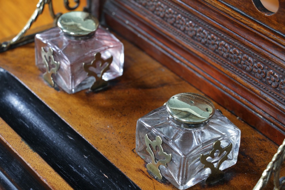 An Edwardian wooden inkstand featuring two glass inkwells, a shaped back gallery with finials, brass side supports, a pen groove, and a lower drawer. View XIII