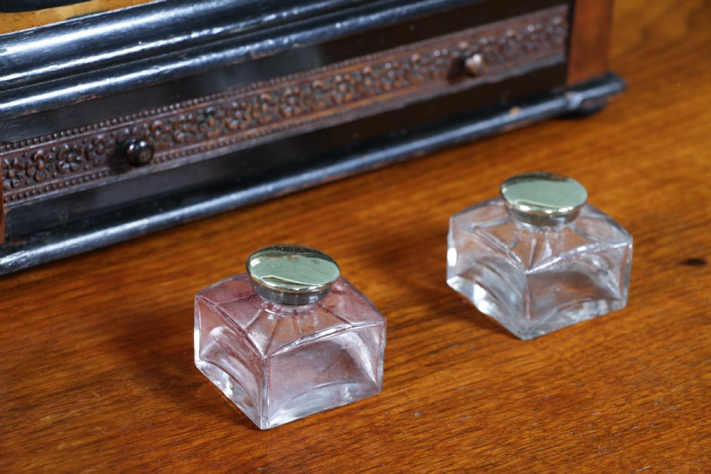 An Edwardian wooden inkstand featuring two glass inkwells, a shaped back gallery with finials, brass side supports, a pen groove, and a lower drawer. View XVI