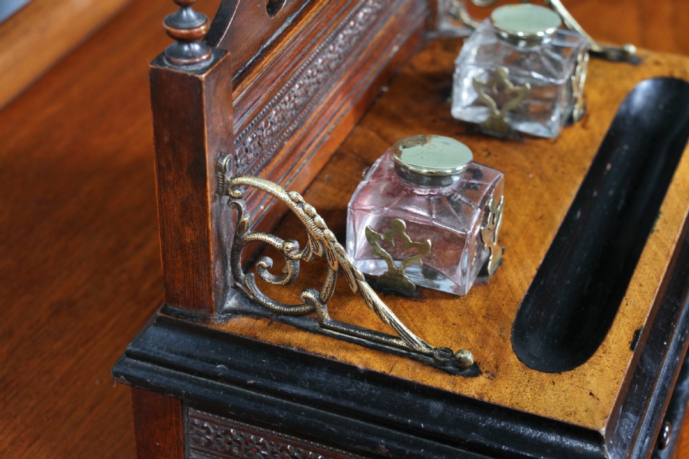 An Edwardian wooden inkstand featuring two glass inkwells, a shaped back gallery with finials, brass side supports, a pen groove, and a lower drawer. View XIX