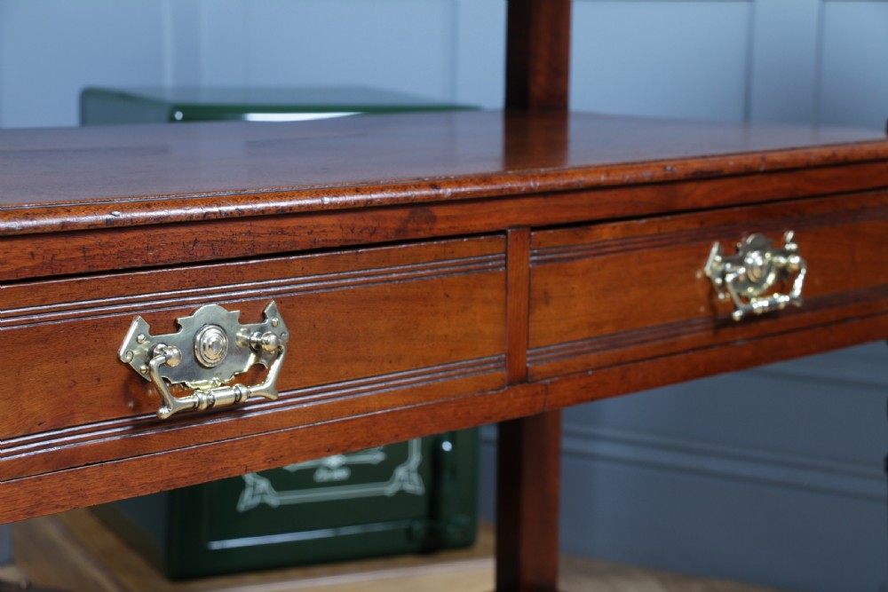 A three-tier Victorian walnut dumb waiter featuring turned columns, carved pediment gallery, two central drawers with brass handles, and brass castors. View VI