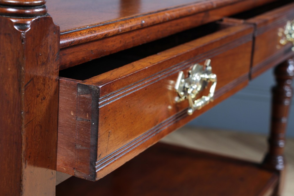 A three-tier Victorian walnut dumb waiter featuring turned columns, carved pediment gallery, two central drawers with brass handles, and brass castors. View VII