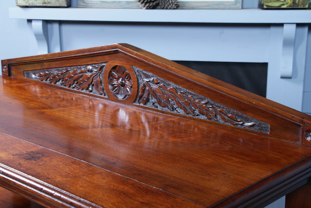 A three-tier Victorian walnut dumb waiter featuring turned columns, carved pediment gallery, two central drawers with brass handles, and brass castors. View VIII