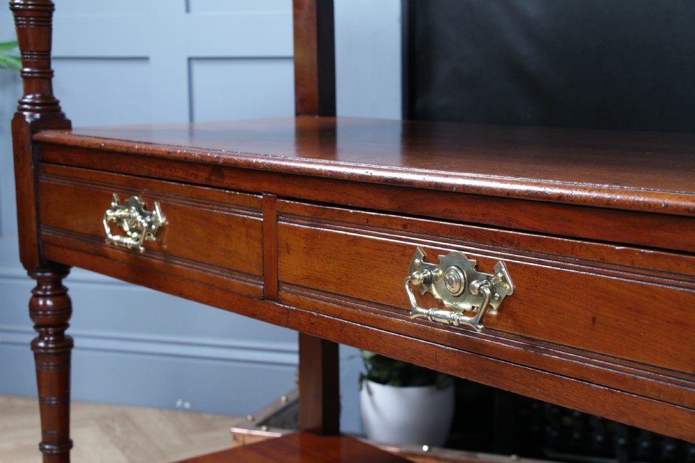 A three-tier Victorian walnut dumb waiter featuring turned columns, carved pediment gallery, two central drawers with brass handles, and brass castors. View IX