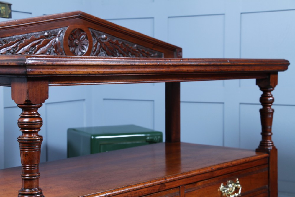 A three-tier Victorian walnut dumb waiter featuring turned columns, carved pediment gallery, two central drawers with brass handles, and brass castors. View XIV