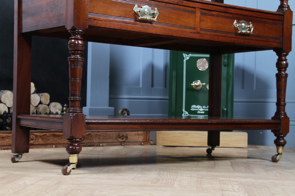 A three-tier Victorian walnut dumb waiter featuring turned columns, carved pediment gallery, two central drawers with brass handles, and brass castors. View XVIII