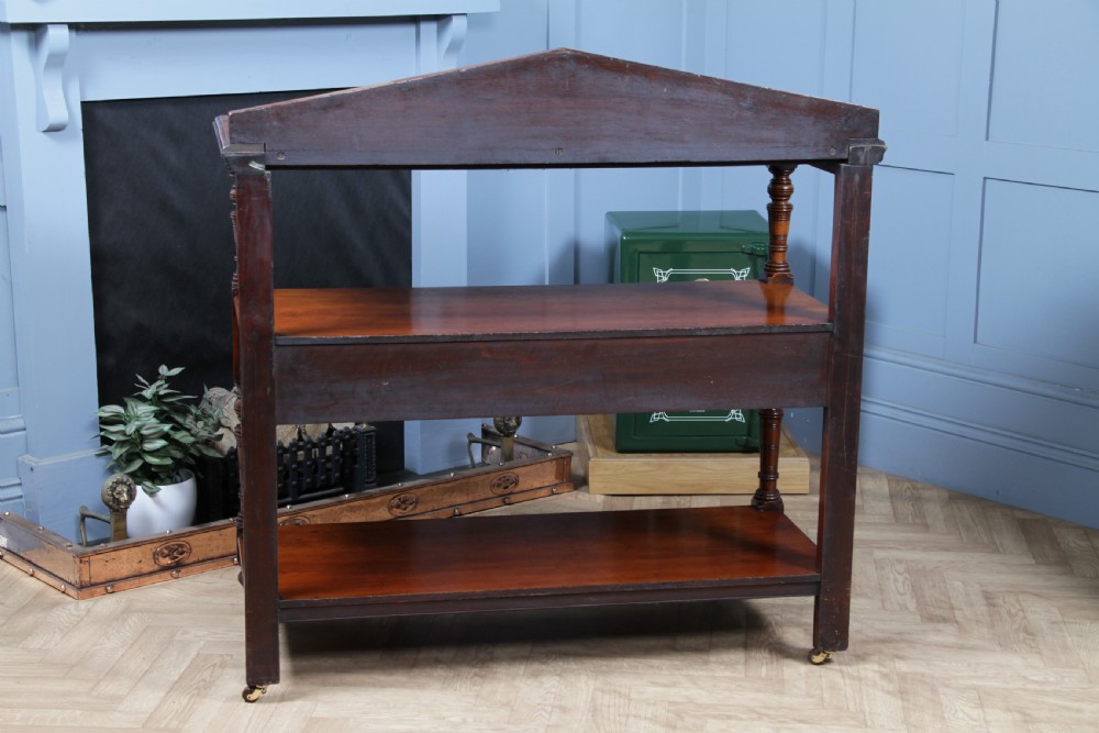 A three-tier Victorian walnut dumb waiter featuring turned columns, carved pediment gallery, two central drawers with brass handles, and brass castors. View XXIII