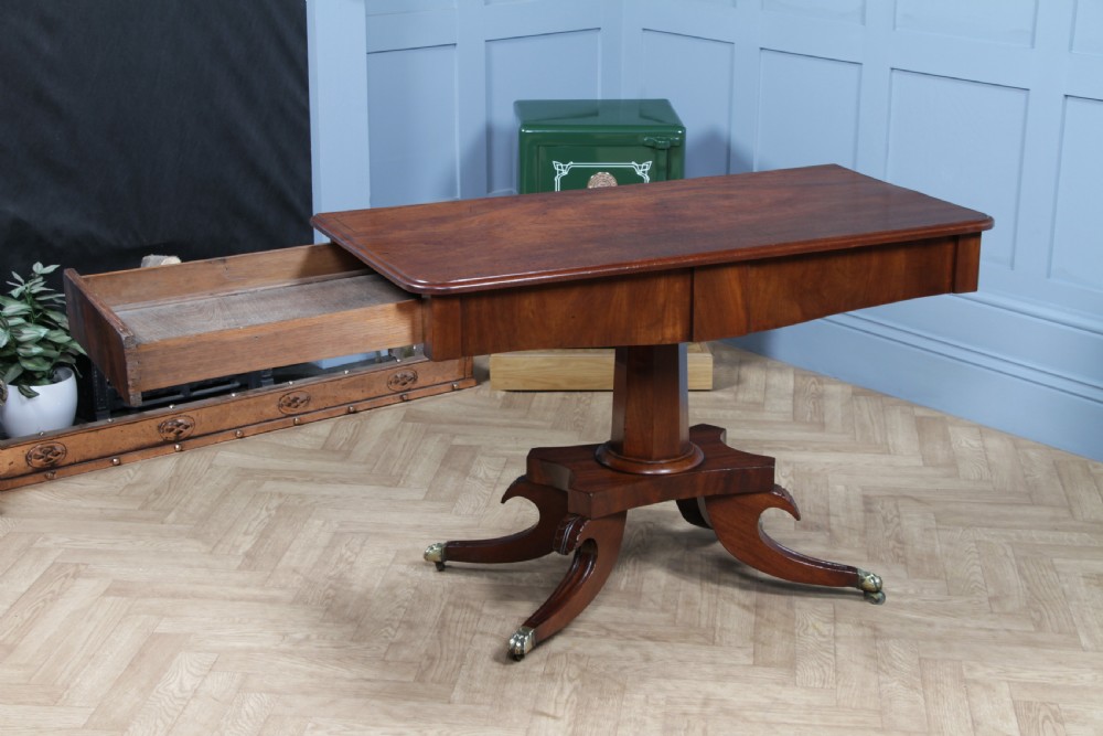 A Regency period mahogany centre table featuring a rectangular top with rounded corners on a central octagonal column and quadform platform base with swept legs. View VII