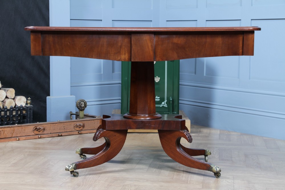 A Regency period mahogany centre table featuring a rectangular top with rounded corners on a central octagonal column and quadform platform base with swept legs. View IX