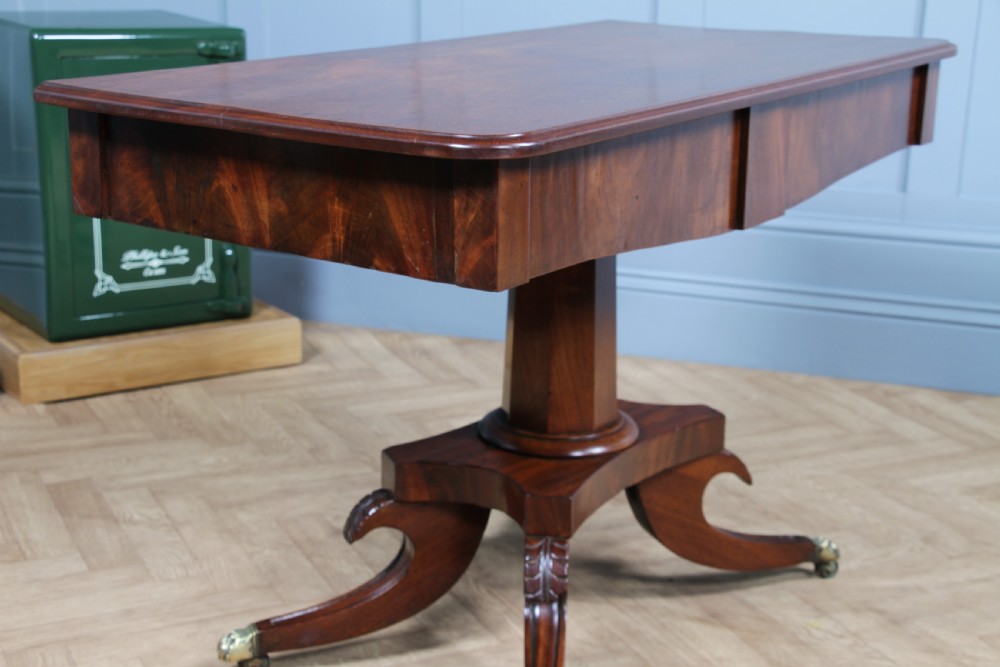 A Regency period mahogany centre table featuring a rectangular top with rounded corners on a central octagonal column and quadform platform base with swept legs. View X