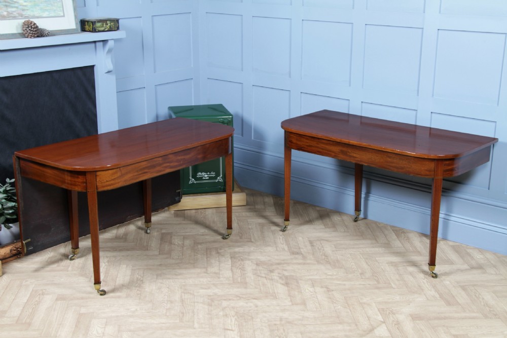 An extended Georgian mahogany dining table featuring semi-circular D-ends, a central drop-leaf section, square tapered legs, and brass castors. View II