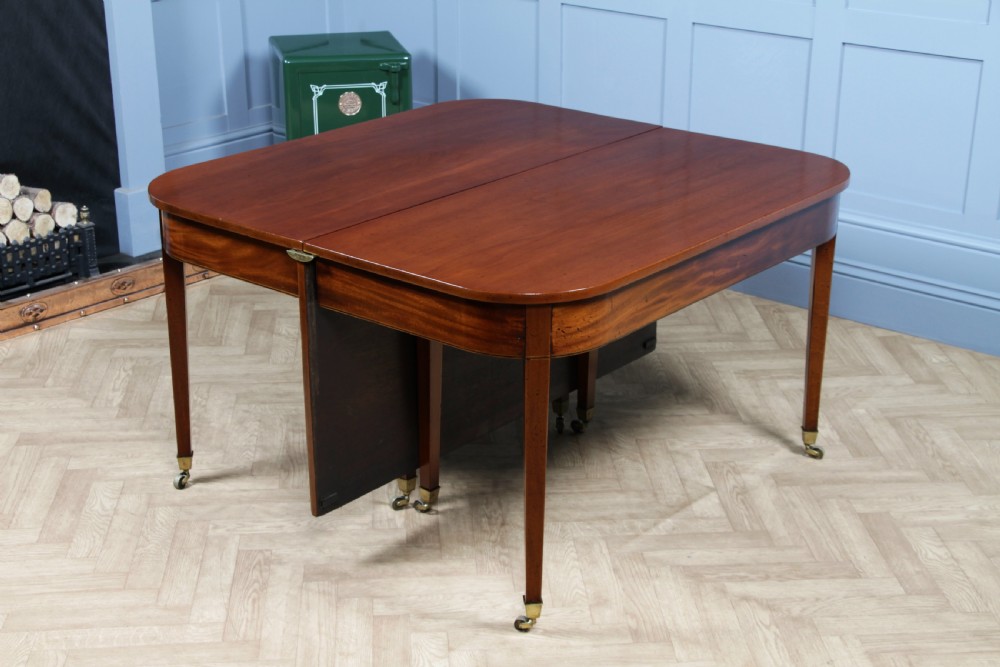 An extended Georgian mahogany dining table featuring semi-circular D-ends, a central drop-leaf section, square tapered legs, and brass castors. View III