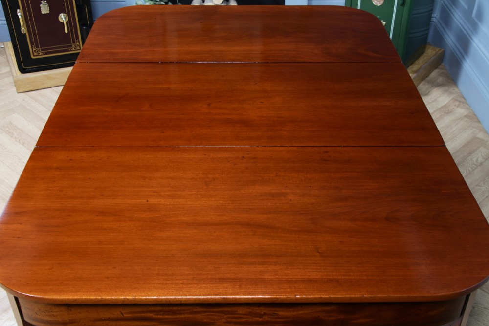 An extended Georgian mahogany dining table featuring semi-circular D-ends, a central drop-leaf section, square tapered legs, and brass castors. View VIII