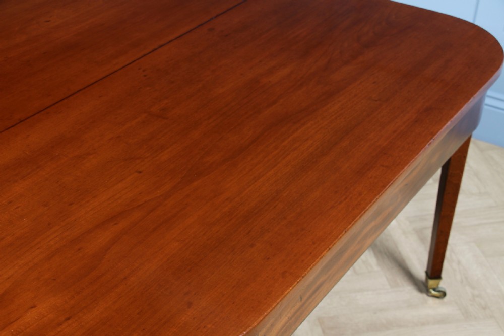 An extended Georgian mahogany dining table featuring semi-circular D-ends, a central drop-leaf section, square tapered legs, and brass castors. View IX