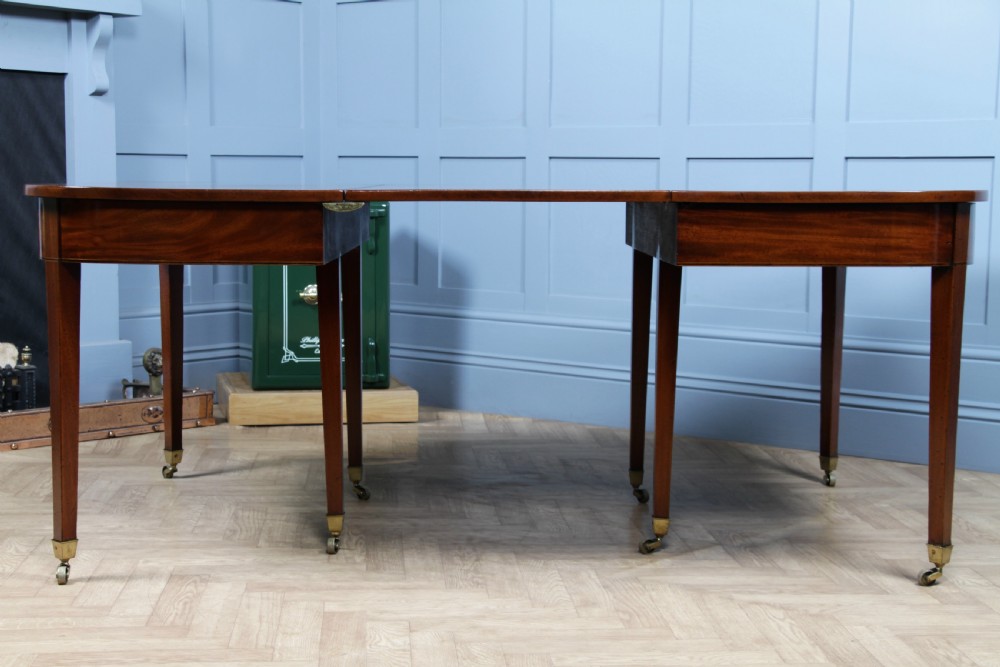 An extended Georgian mahogany dining table featuring semi-circular D-ends, a central drop-leaf section, square tapered legs, and brass castors. View XI
