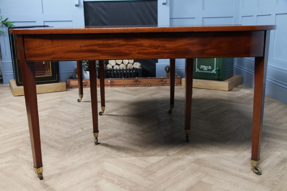 An extended Georgian mahogany dining table featuring semi-circular D-ends, a central drop-leaf section, square tapered legs, and brass castors. View XV