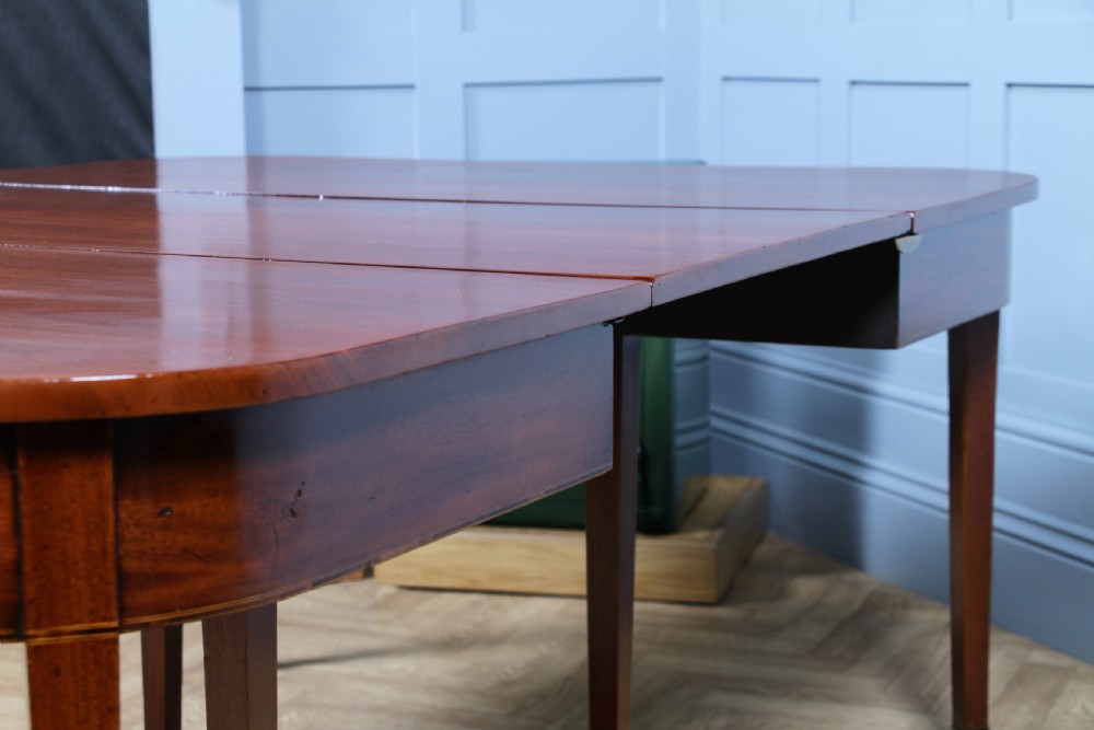 An extended Georgian mahogany dining table featuring semi-circular D-ends, a central drop-leaf section, square tapered legs, and brass castors. View XVI