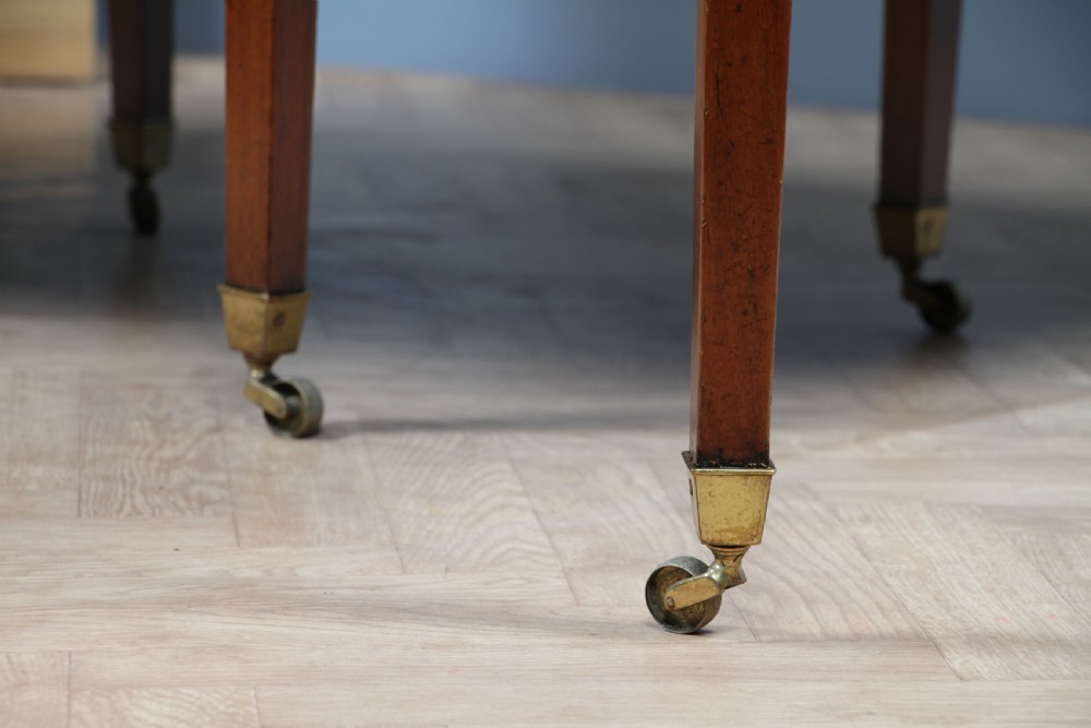 An extended Georgian mahogany dining table featuring semi-circular D-ends, a central drop-leaf section, square tapered legs, and brass castors. View XVII
