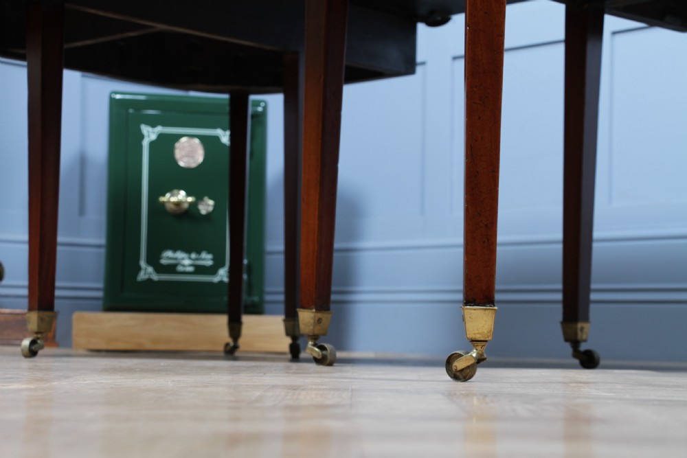 An extended Georgian mahogany dining table featuring semi-circular D-ends, a central drop-leaf section, square tapered legs, and brass castors. View XVIII