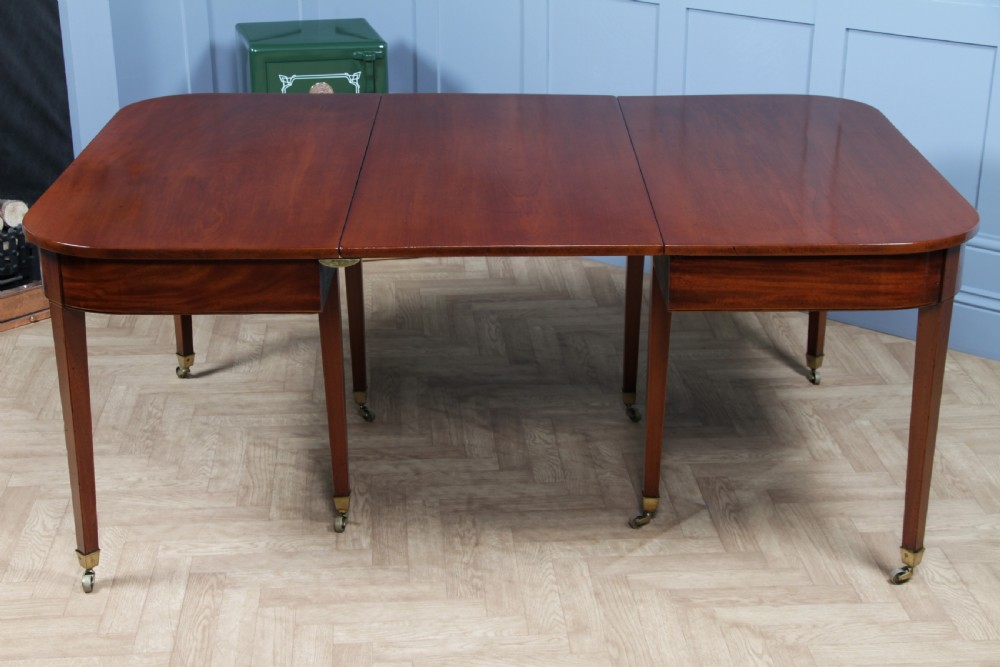 An extended Georgian mahogany dining table featuring semi-circular D-ends, a central drop-leaf section, square tapered legs, and brass castors. View XXII